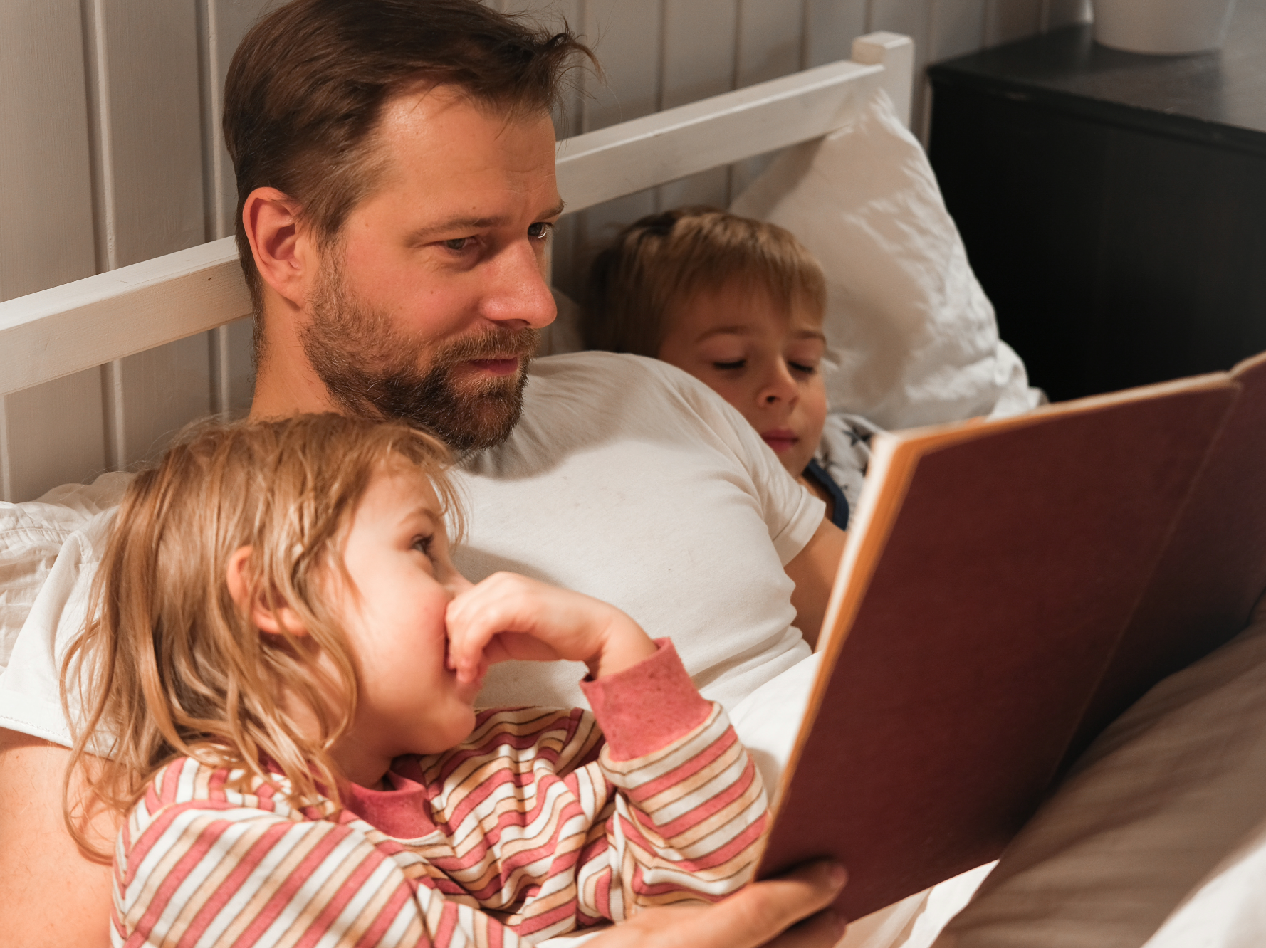 Vater liest mit zwei Kindern gemeinsam ein Buch im Bett.