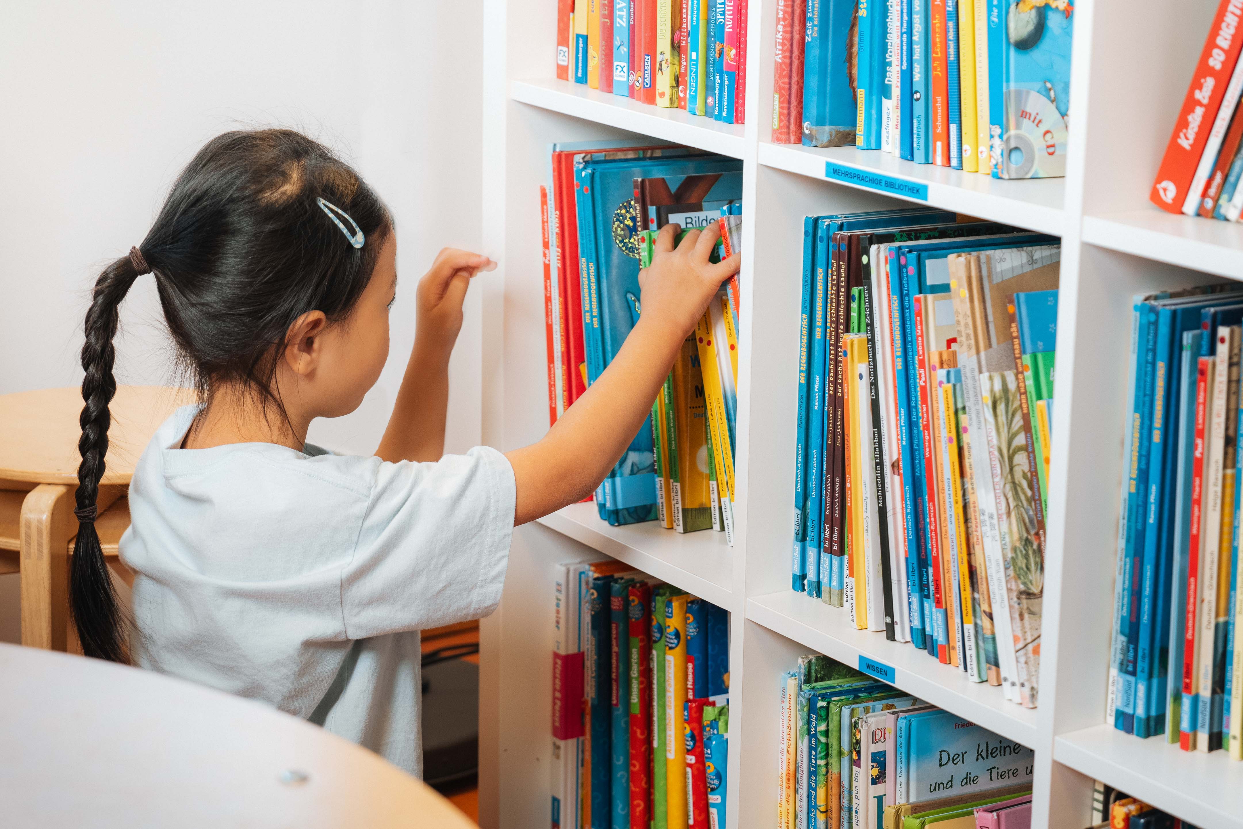 Mädchen sucht sich ein Buch in einem Bücherregal aus