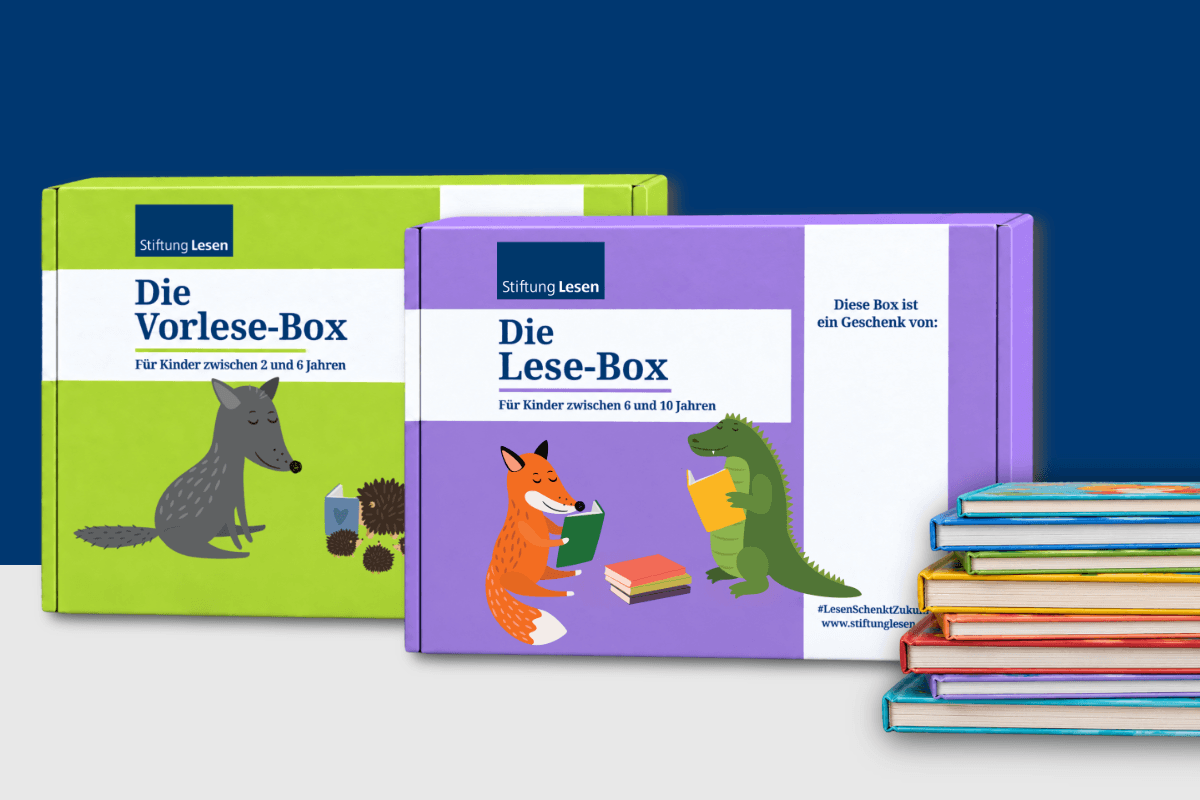 Grüne Vorlese-Box für Kinder von zwei bis sechs Jahren und lilafarbene Lese-Box für Kinder von sechs bis zehn Jahren der Stiftung Lesen. Die Boxen sind mit illustrierten Tieren und Büchern gestaltet; rechts daneben liegt ein Stapel bunter Bücher.