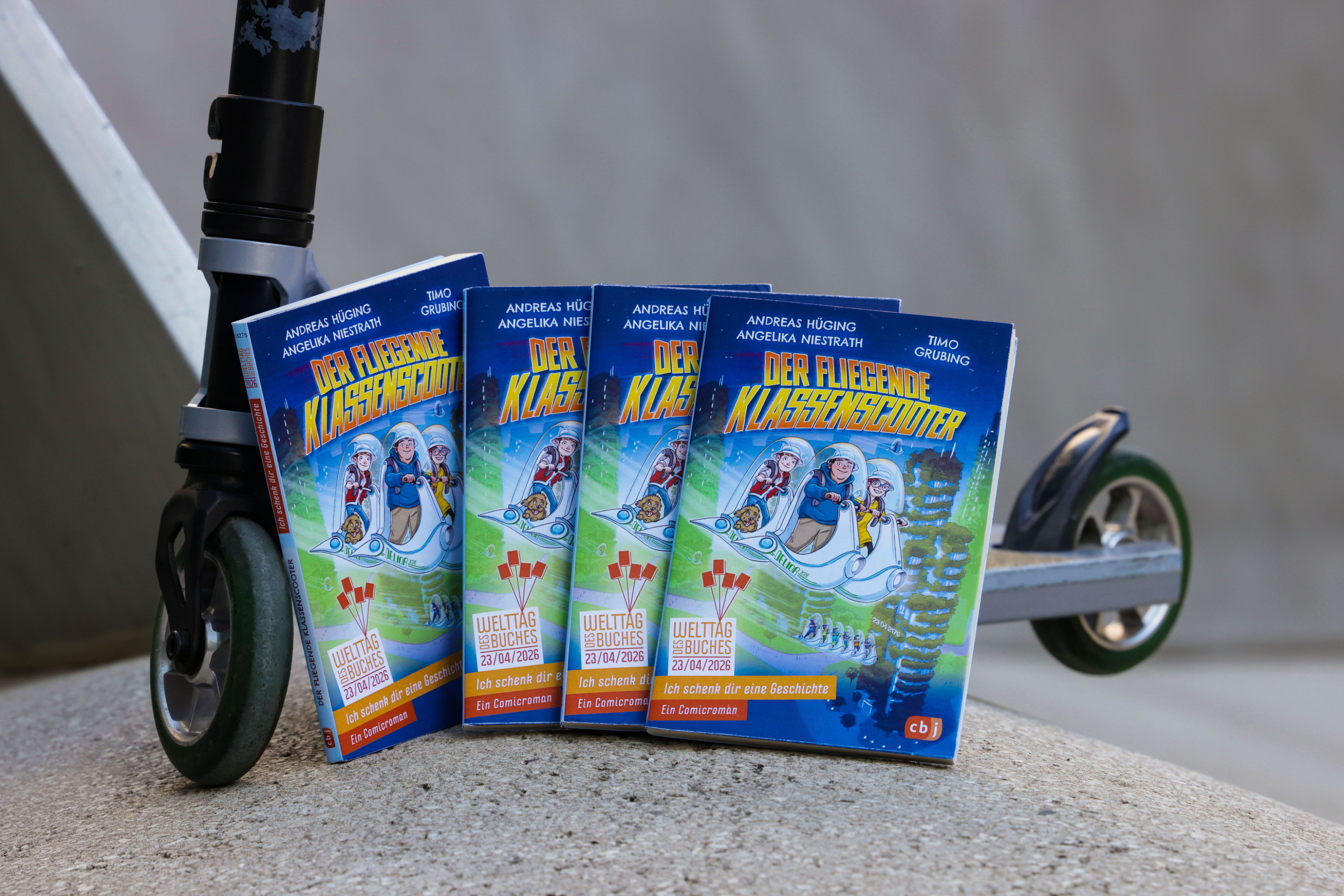 Fünf Exemplare des Buches „Der fliegende Klassenscooter“ lehnen an der Vorderseite eines Rollers. Die Bücher stehen fächerförmig aufgereiht auf dem Boden. Das Cover zeigt Kinder in futuristischen Helmen auf einem schwebenden Scooter.