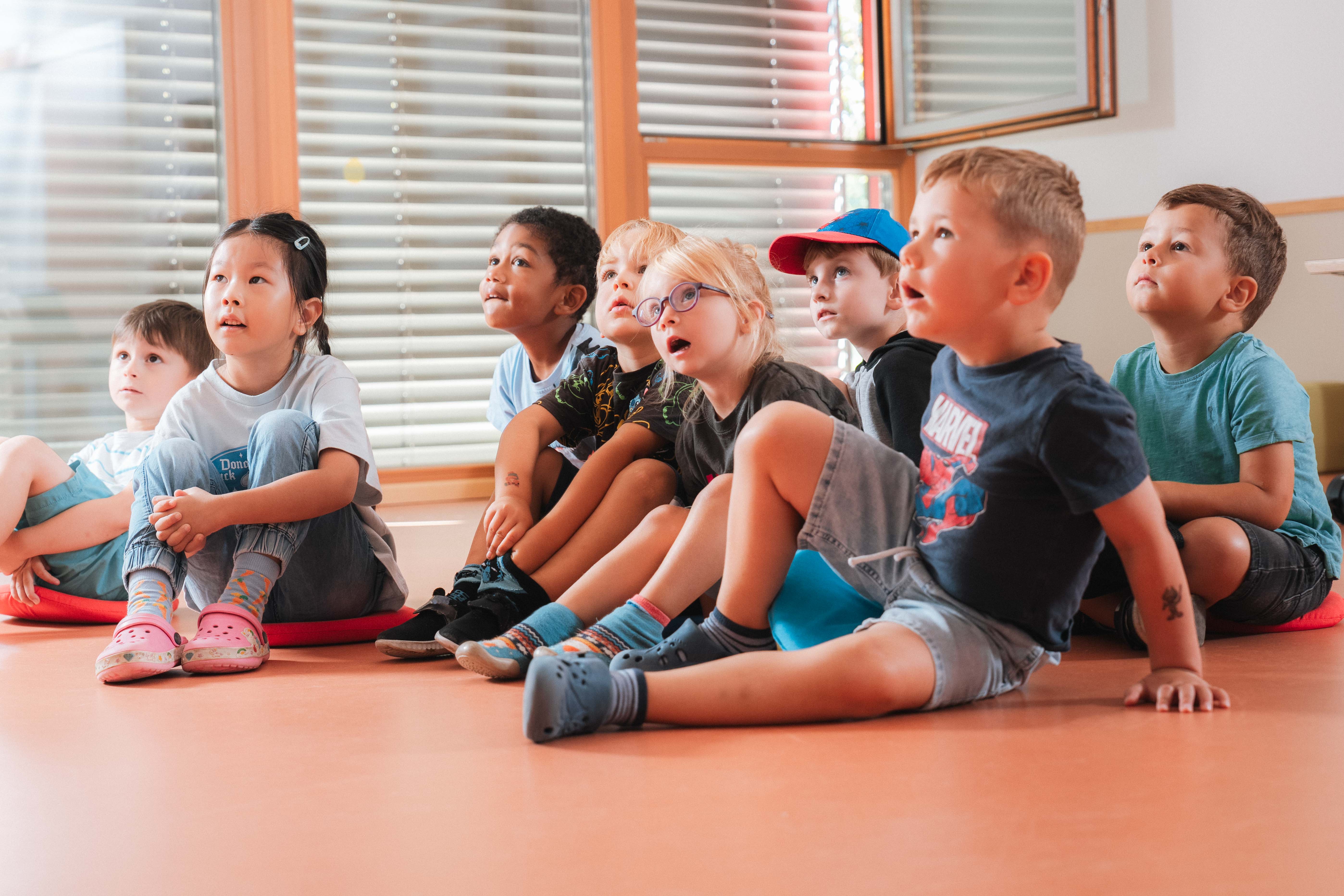 Kinder sitzen auf dem Boden und hören beim Vorlesen zu