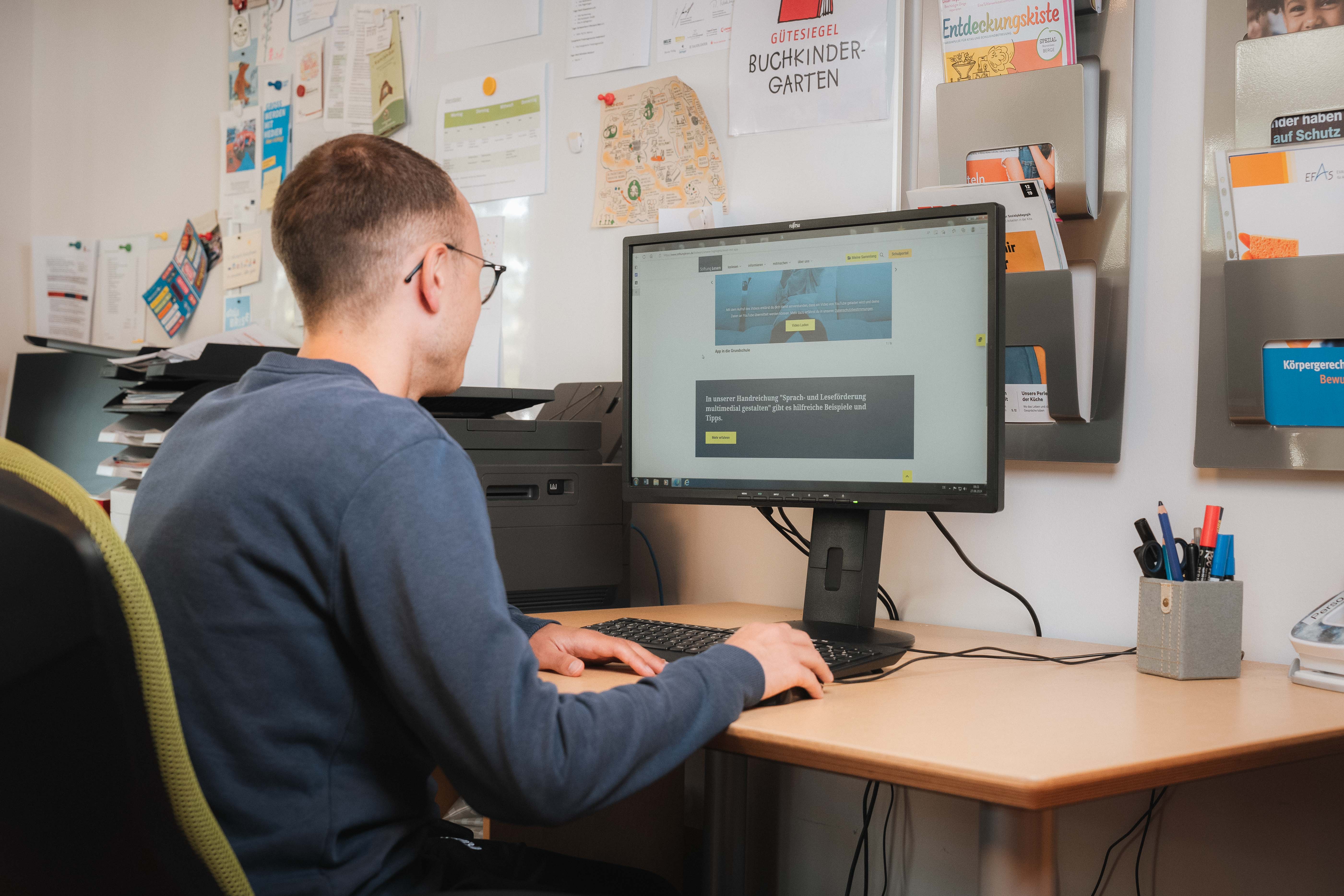 Ein Mann sitzt vor dem Computer und schaut sich das Kitaportal der Stiftung Lesen an