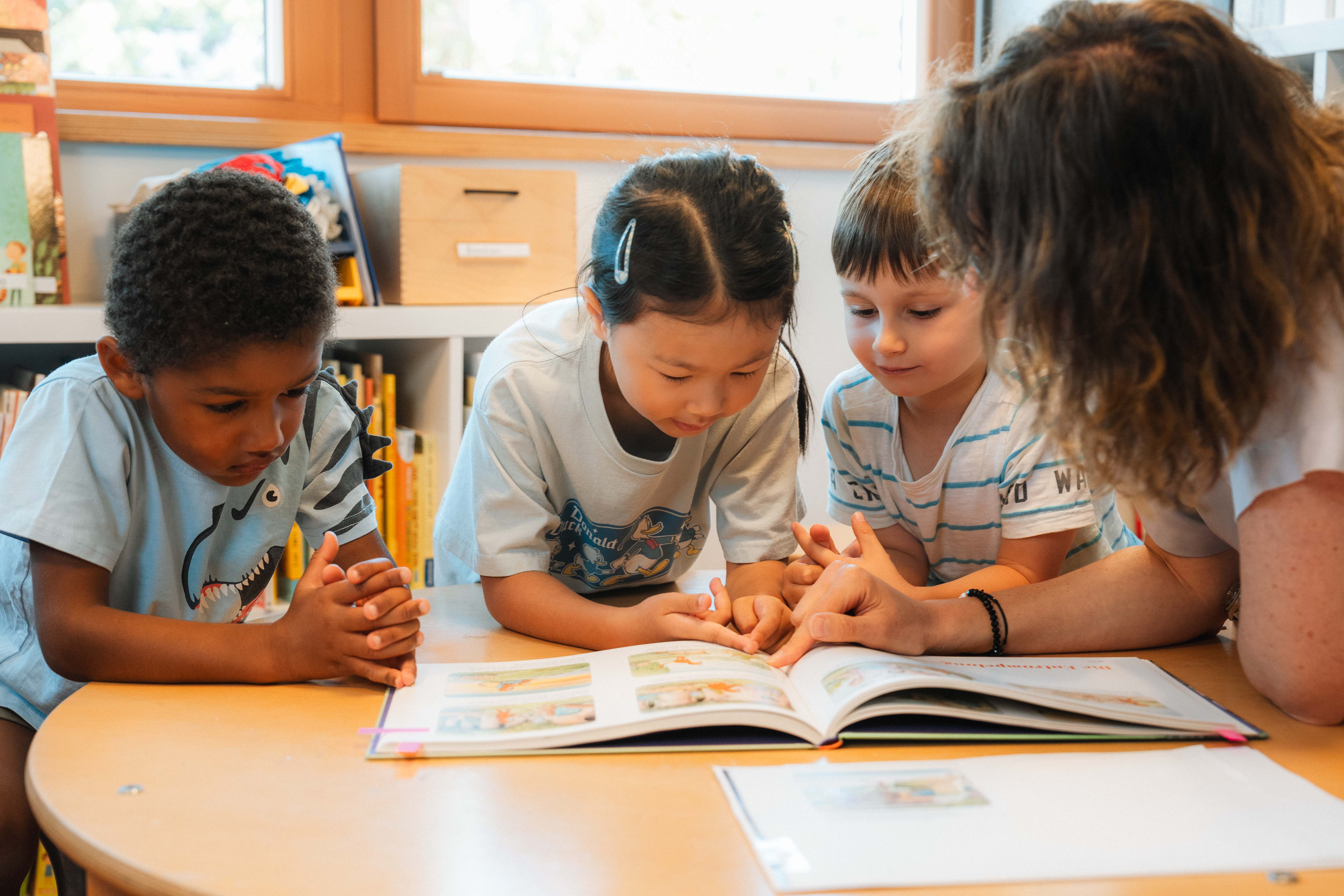 Drei Kinder und eine Kitafachkraft lesen ein Buch