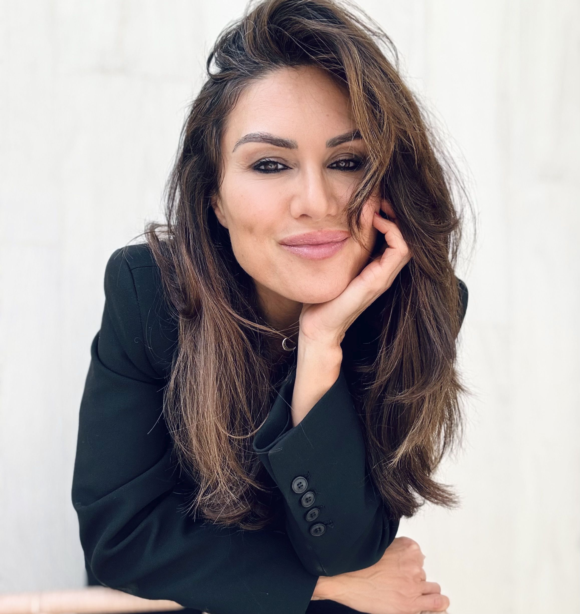 Porträt einer lächelnden Frau (Moderatorin Nazan Eckes) mit langen braunen Haaren, die ihren Kopf entspannt auf die Hand stützt und in die Kamera blickt.