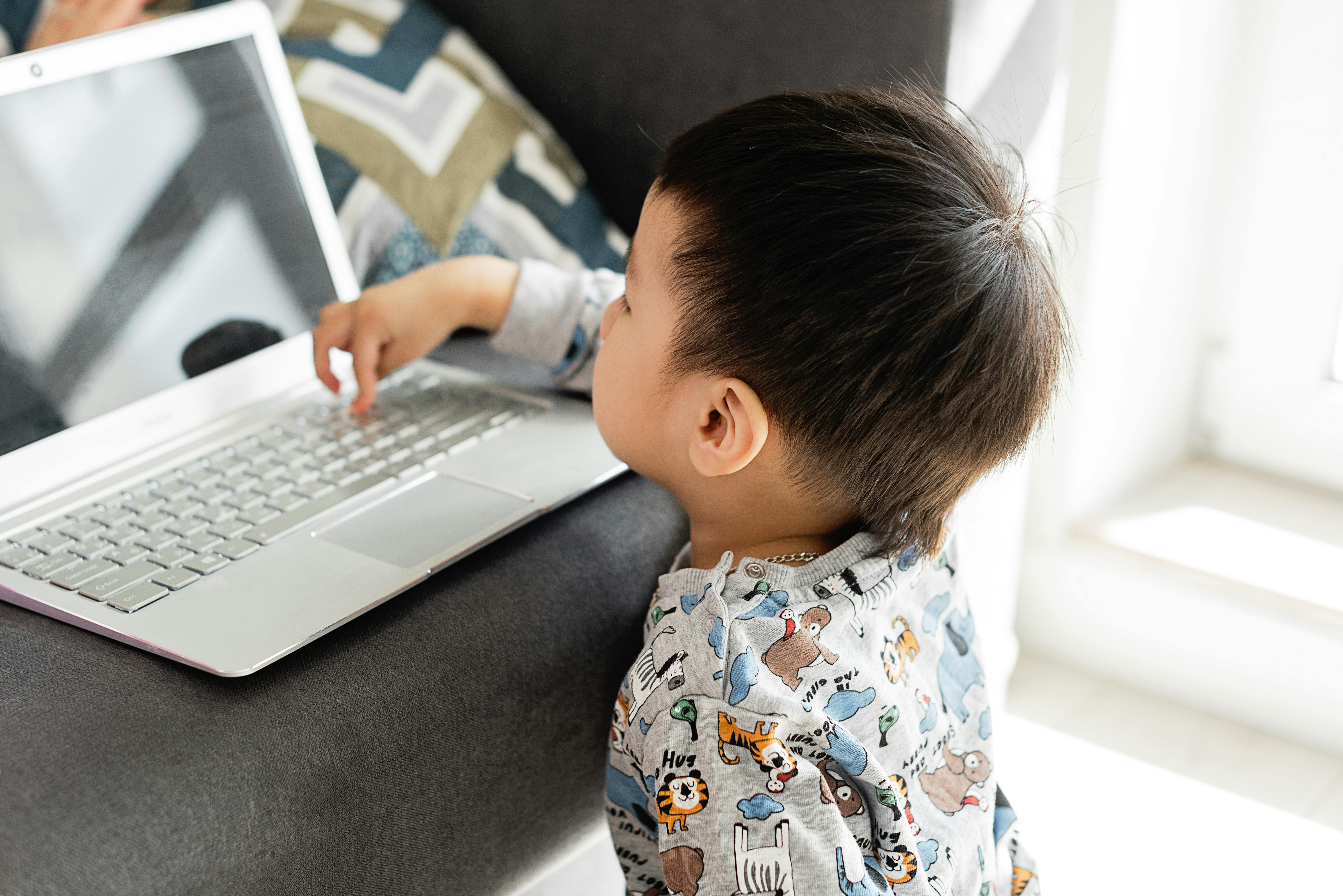 Ein zweijähriges Kind sitzt vor einem Laptop und tippt auf der Tastatur herum.