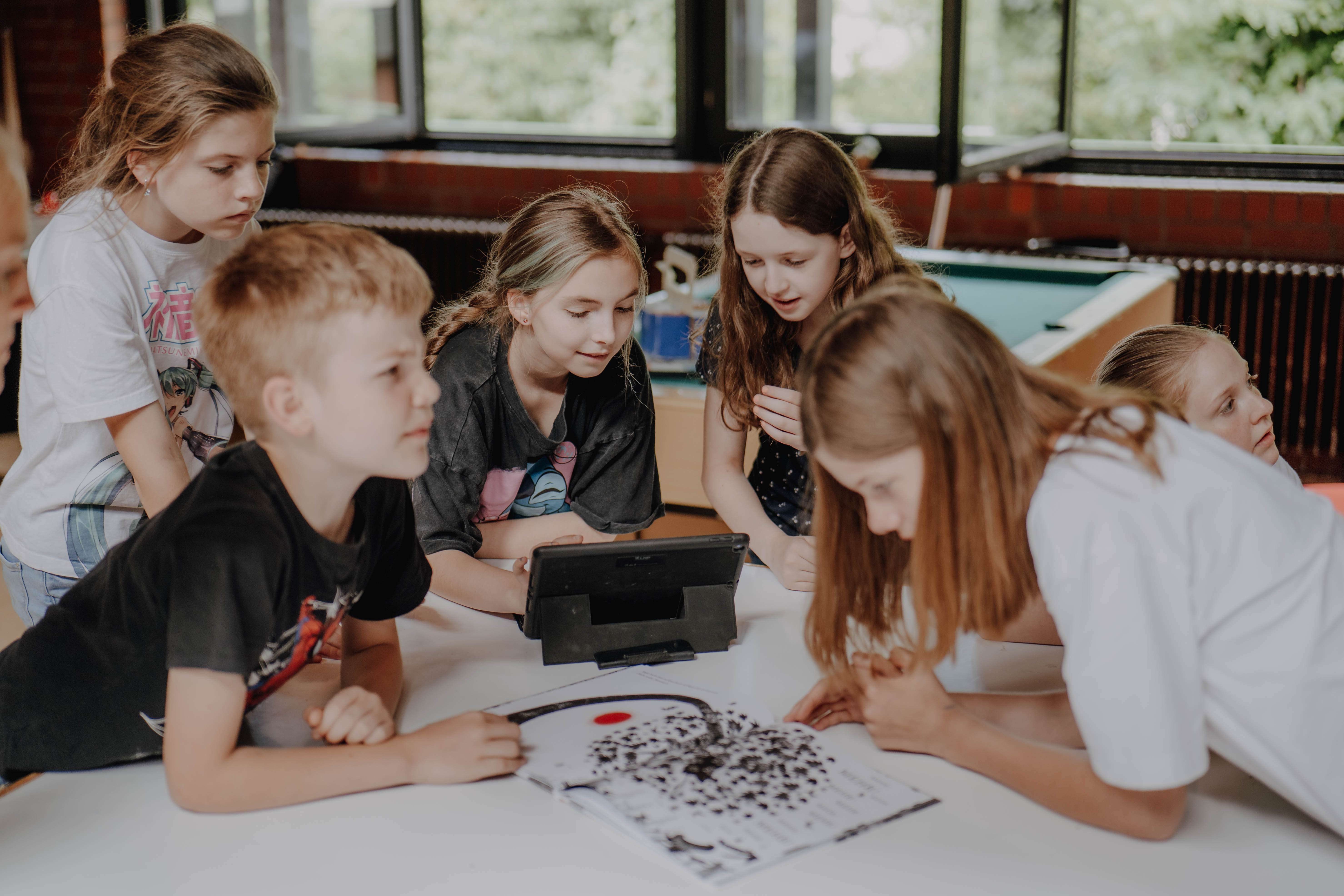 Kinder und Jugendliche sitzen in einem Leseclub um einen Tisch herum und beschäftigen sich mit verschiedenen Medien.