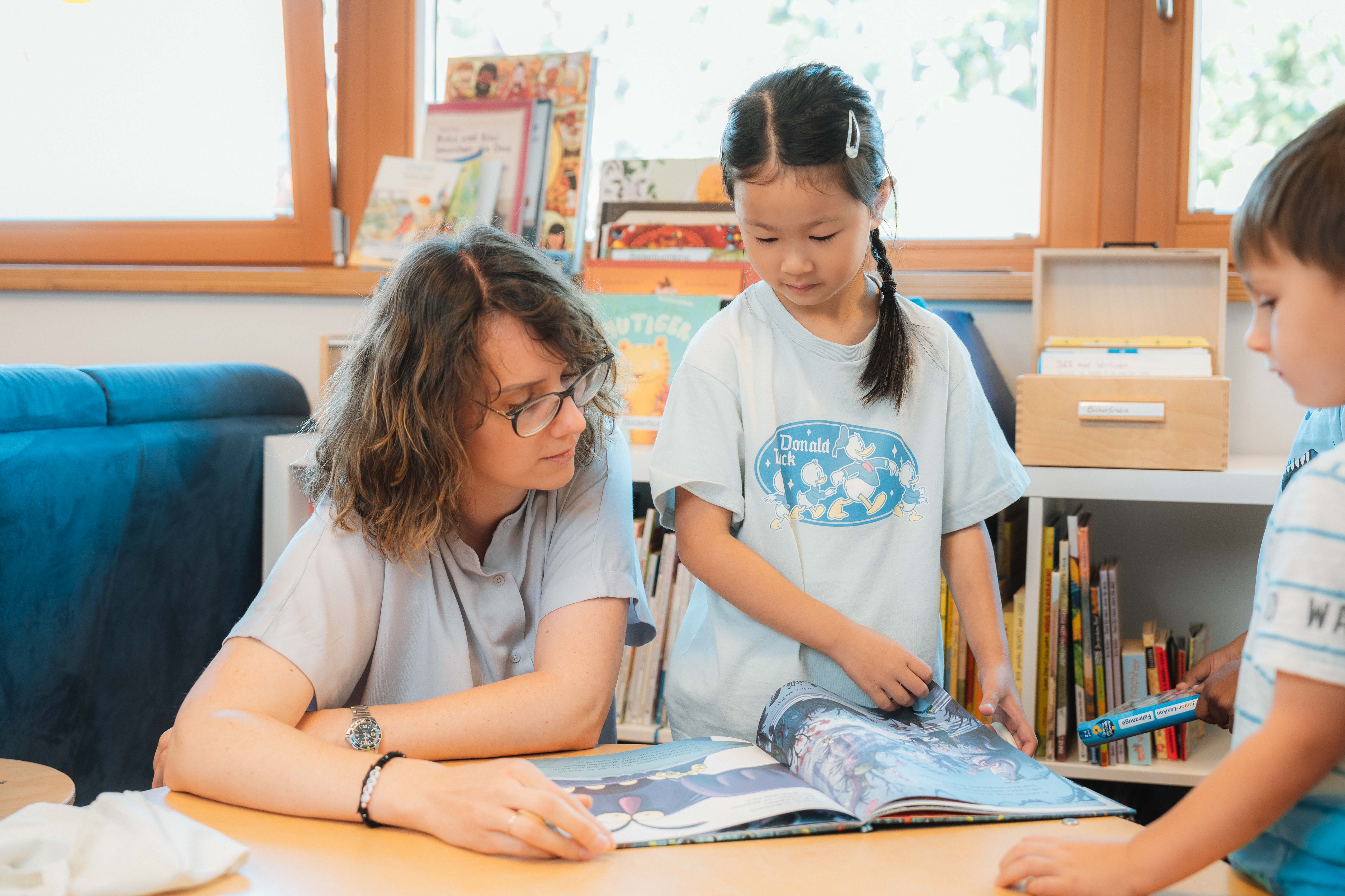 Eine pädagogische Fachkraft blättert mimt zwei Kindergartenkindern in einem Buch