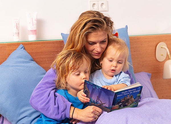 Eine Mutter sitzt mit zwei frisch gebadeten Kindern im Bett und liest