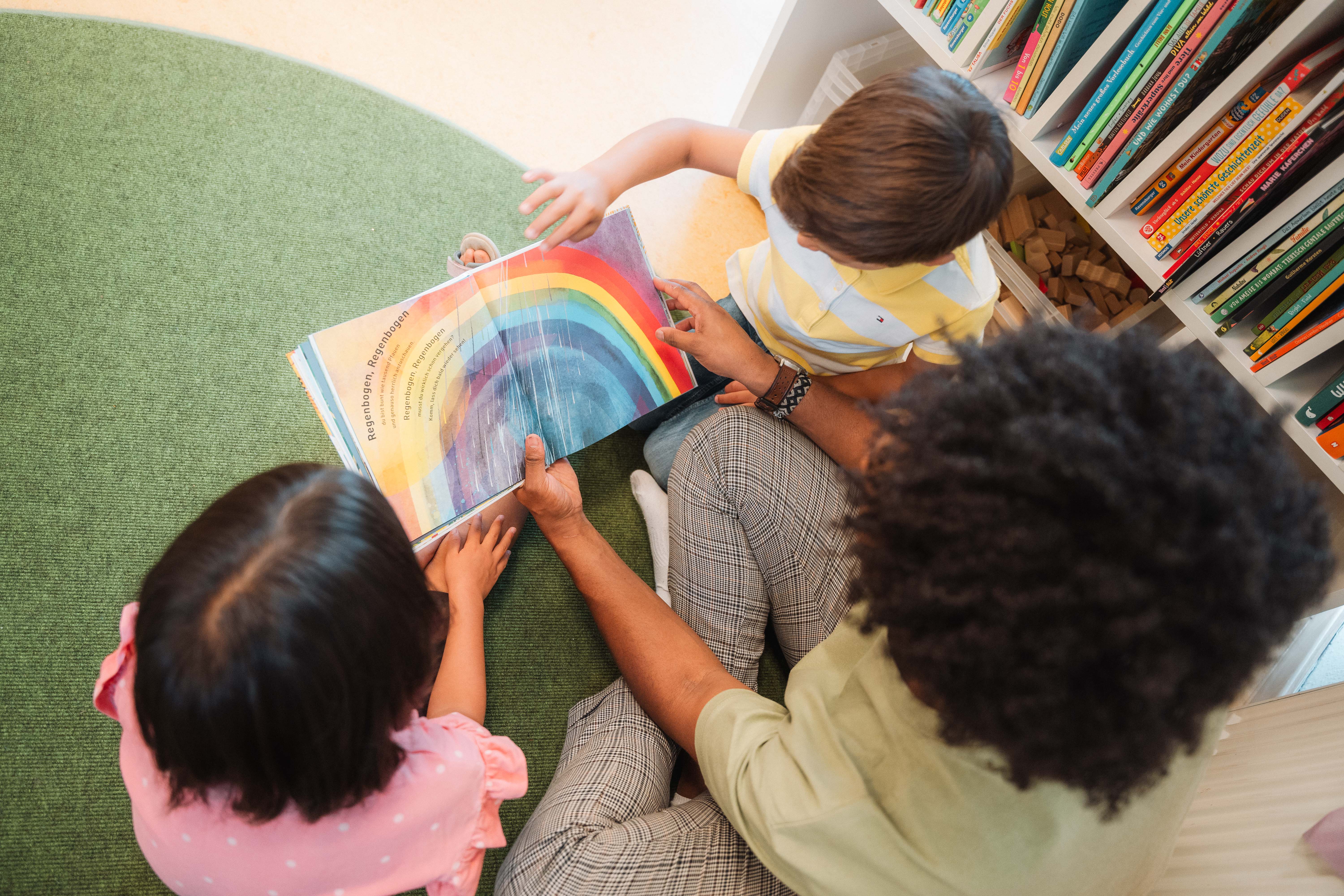 Kinder beim Blättern in einem Bilderbuch mit Regenbogen