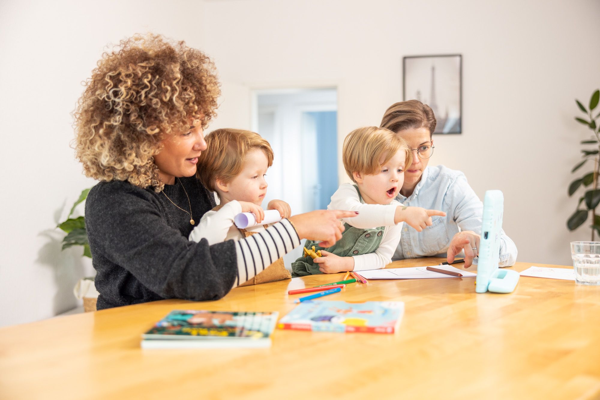 Zwei erwachsene Frauen lesen mit zwei Kindern auf dem Tablet in der App Einfach Vorlesen.