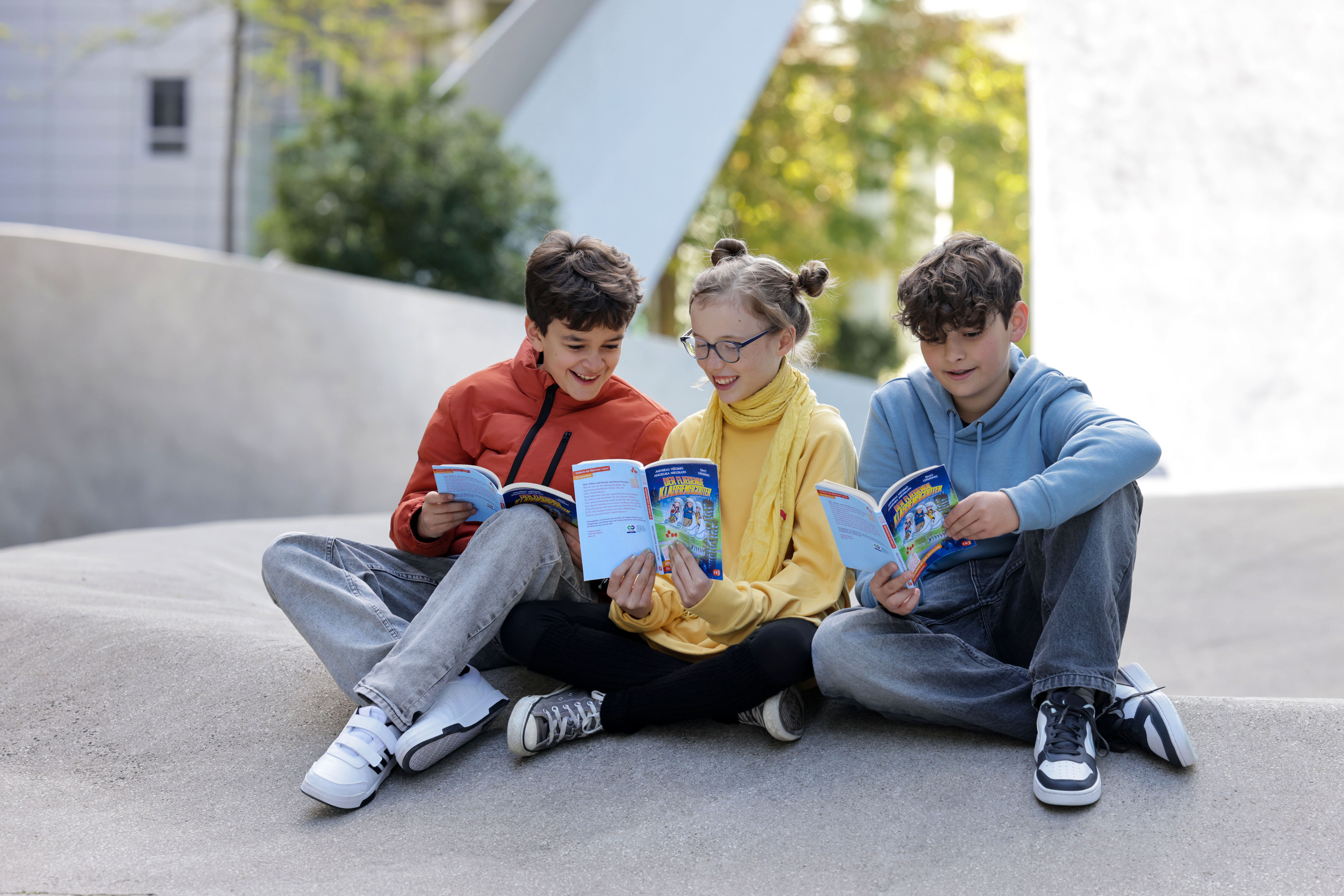 Drei Kinder sitzen draußen zusammen und lesen Bücher, ein Motiv für Leseförderung und gemeinsame Lesezeit