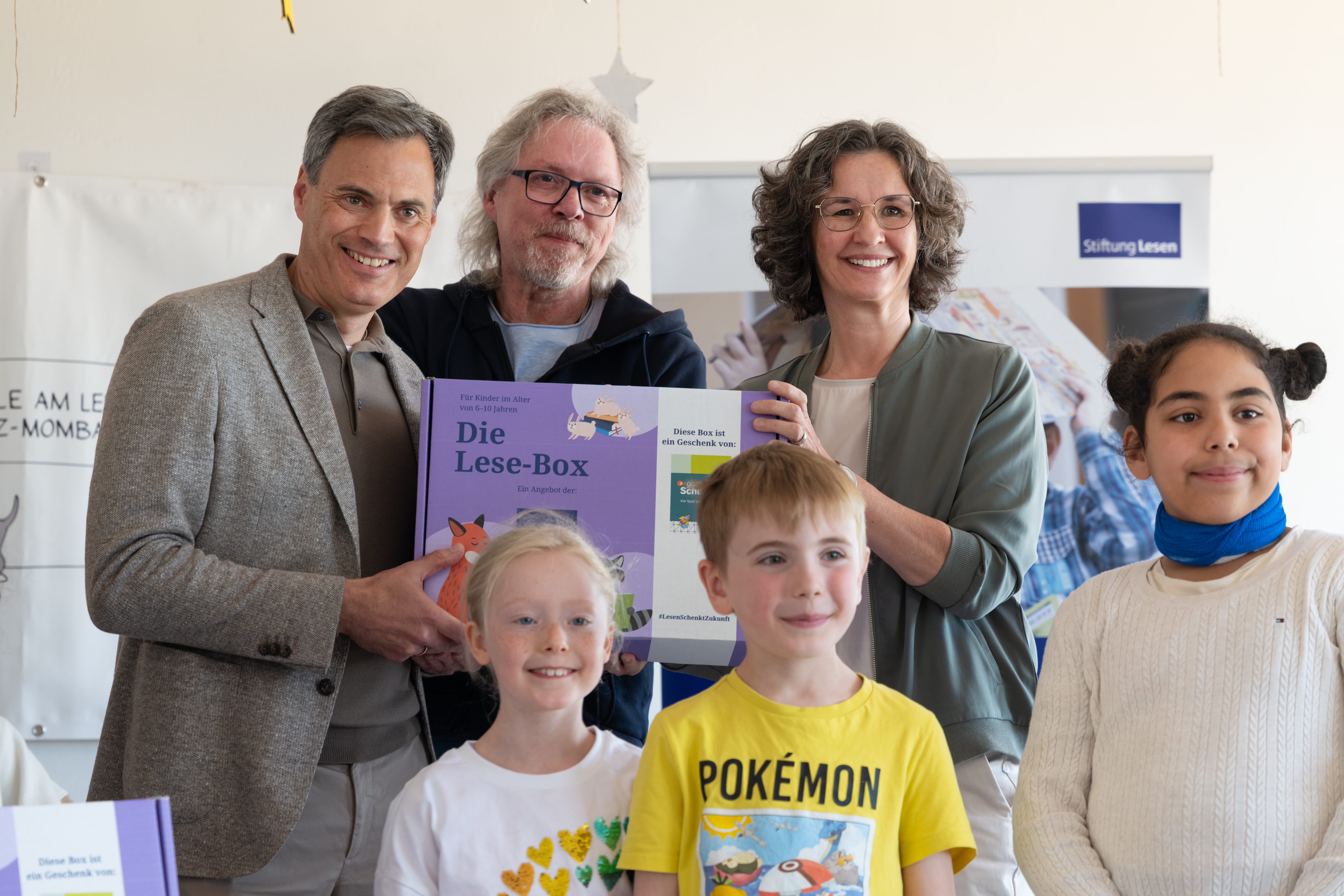 Kinder und Erwachsene stehen gemeinsam mit zwei Lese-Boxen der Stiftung Lesen in einem Veranstaltungsraum.
