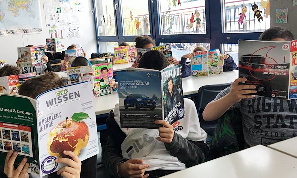Schülerinnen und Schüler lesen im Klassenzimmer verschiedene Kinder- und Jugendzeitschriften