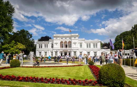 Blick auf die Villa Hammerschmidt mit Gartenanlage und zahlreichen Besucherinnen und Besuchern bei einer Veranstaltung im Freien.