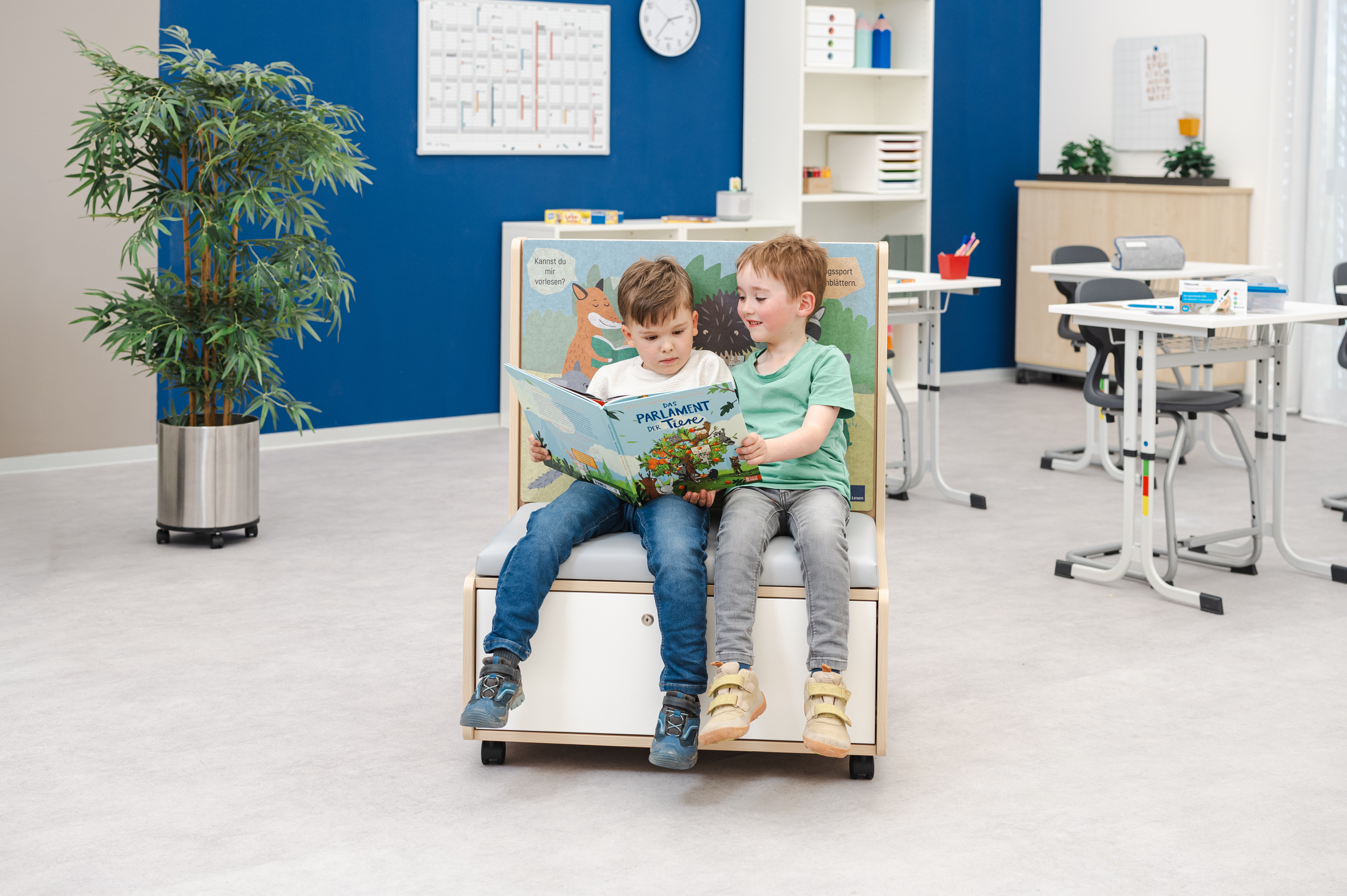 Zwei Kinder sitzen auf einem Lese-Möbel und schauen gemeinsam in ein Buch