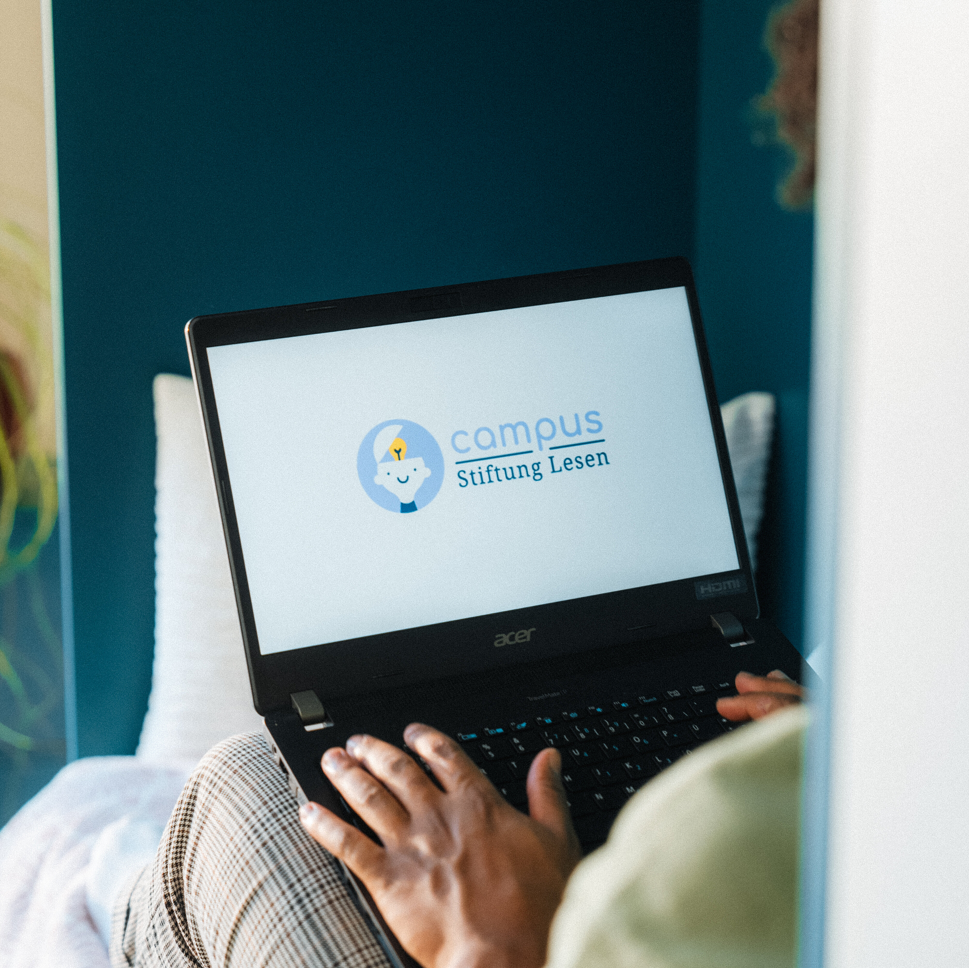 Person sitzt mit einem Laptop auf dem Schoß; auf dem Bildschirm ist das Logo „campus Stiftung Lesen“ zu sehen.