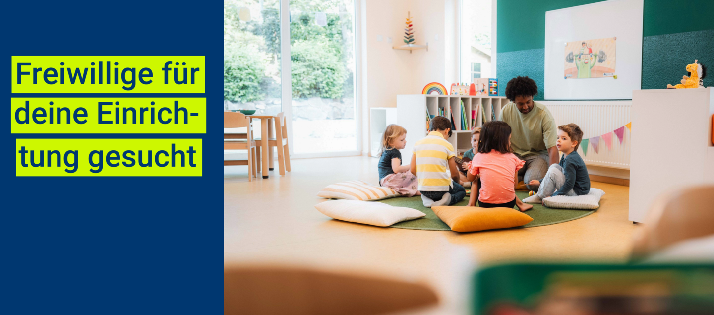 Banner mit dem Schriftzug „Freiwillige für deine Einrichtung gesucht“ auf blauem Hintergrund; rechts sitzt ein Mann mit mehreren Kindern im Kindergarten auf Kissen im Kreis und liest bzw. spricht mit ihnen in einem hellen Gruppenraum.
