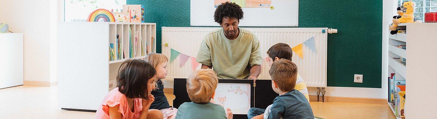 Vorlesesituation: Mann liest einer Gruppe von Kindern aus einem Kamishibai vor