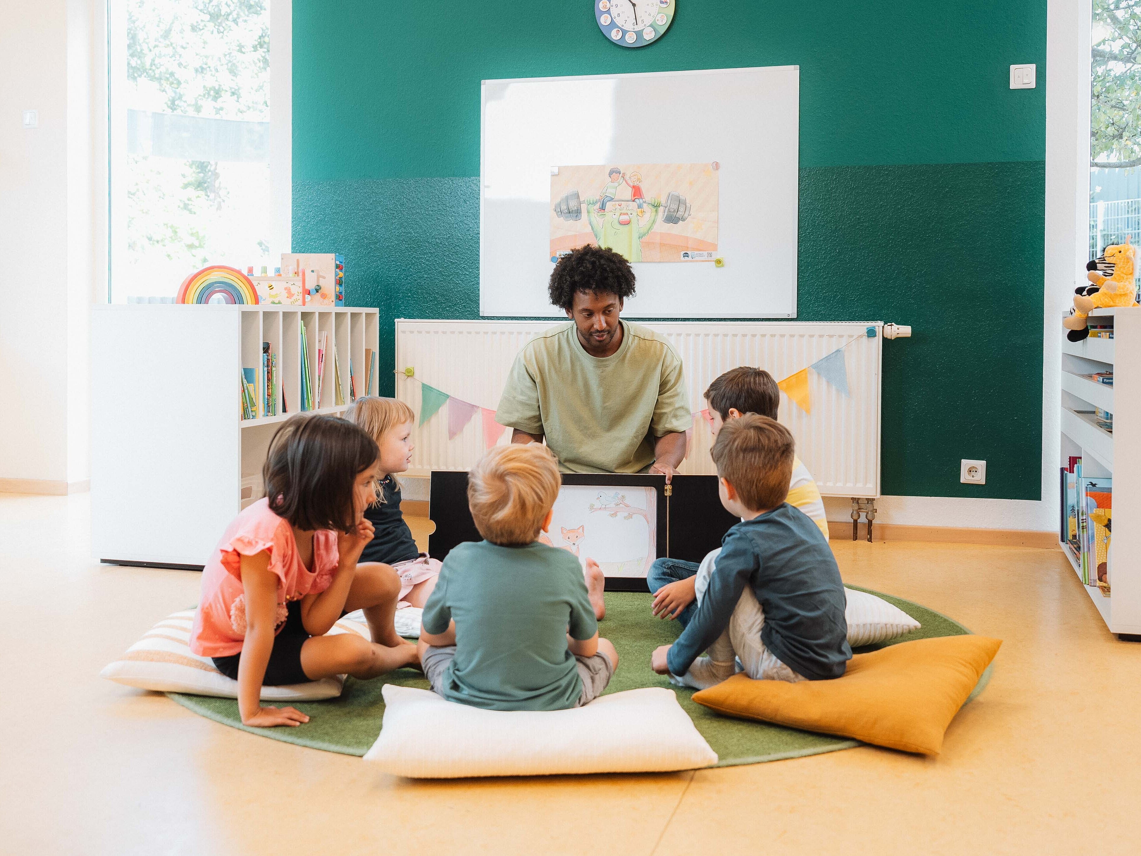 Vorlesesituation: Mann liest einer Gruppe von Kindern aus einem Kamishibai vor