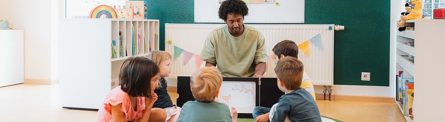 Vorlesesituation: Mann liest einer Gruppe von Kindern aus einem Kamishibai vor