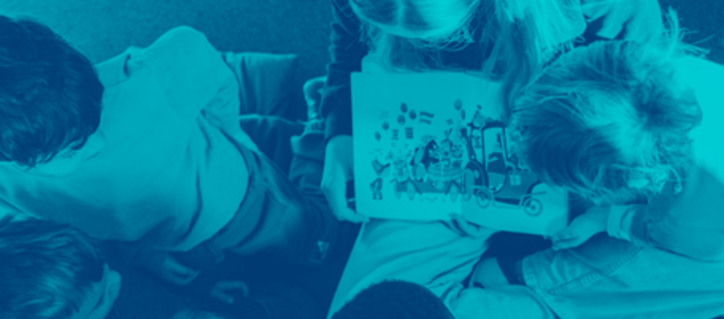 Kinder sitzen im Kreis und bekommen vorgelesen, in der Mitte ist ein aufgeschlagenes Buch