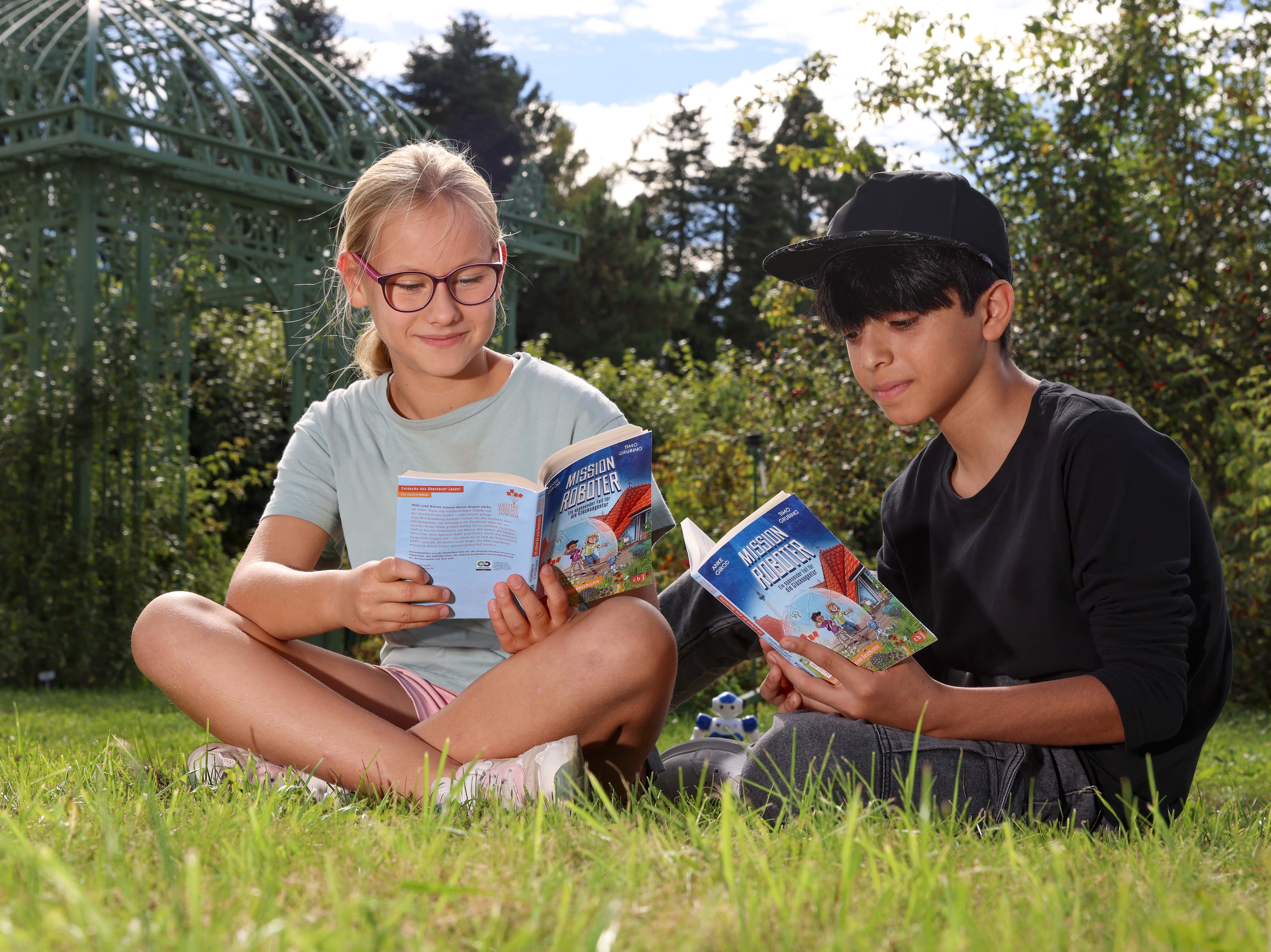 Ein Mädchen und ein Junge sitzen im Gras und lesen ein Buch