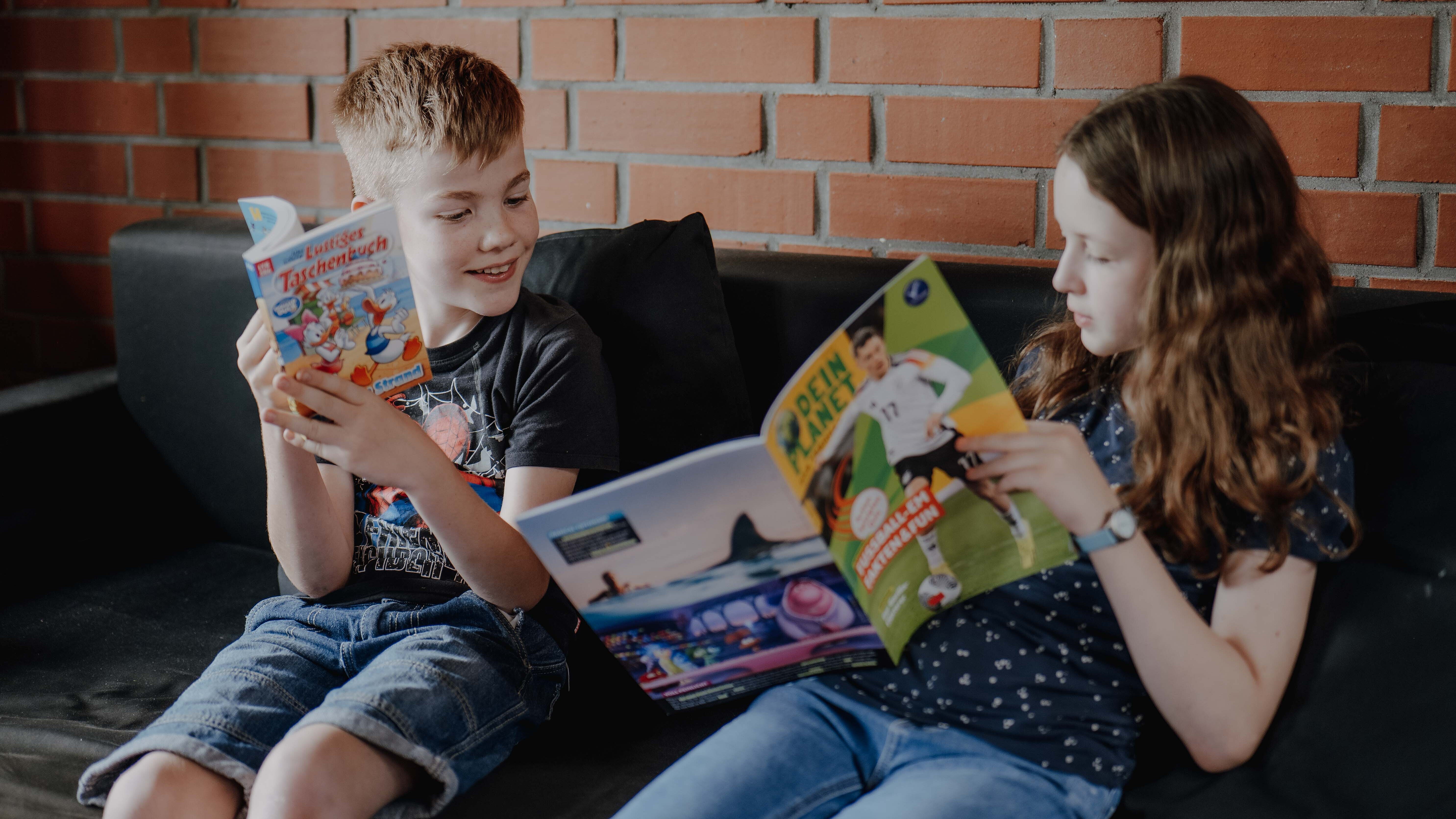 Mädchen und Junge lesen gemeinsam in einem Buch und einer Zeitschrift