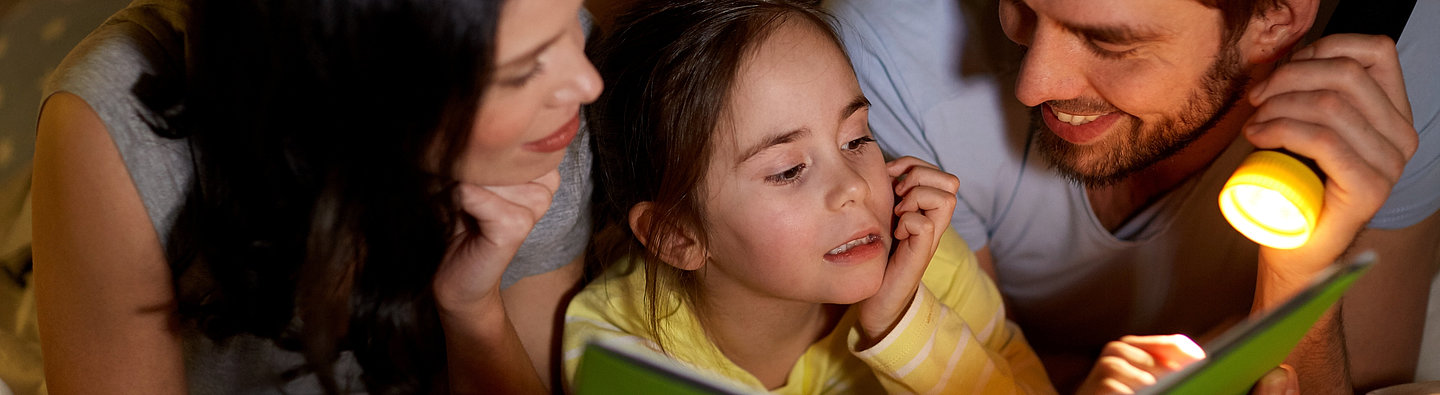 Mutter und Vater lesen Tochter mit Taschenlampe vor