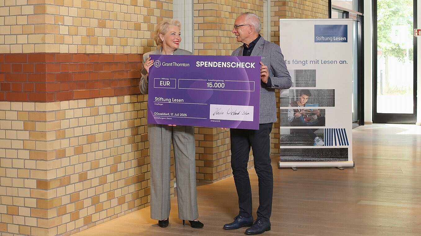  Prof. Dr. Heike Wieland-Blöse, CEO Grant Thornton in Deutschland, steht mit Dr. Jörg F. Maas, Hauptgeschäftsführer der Stiftung Lesen, in einem modernen Gebäude. Sie halten gemeinsam einen übergroßen Spendenscheck über 15.000 Euro mit dem Logo von Grant Thornton Deutschland. Der Scheck ist an die Stiftung Lesen adressiert.