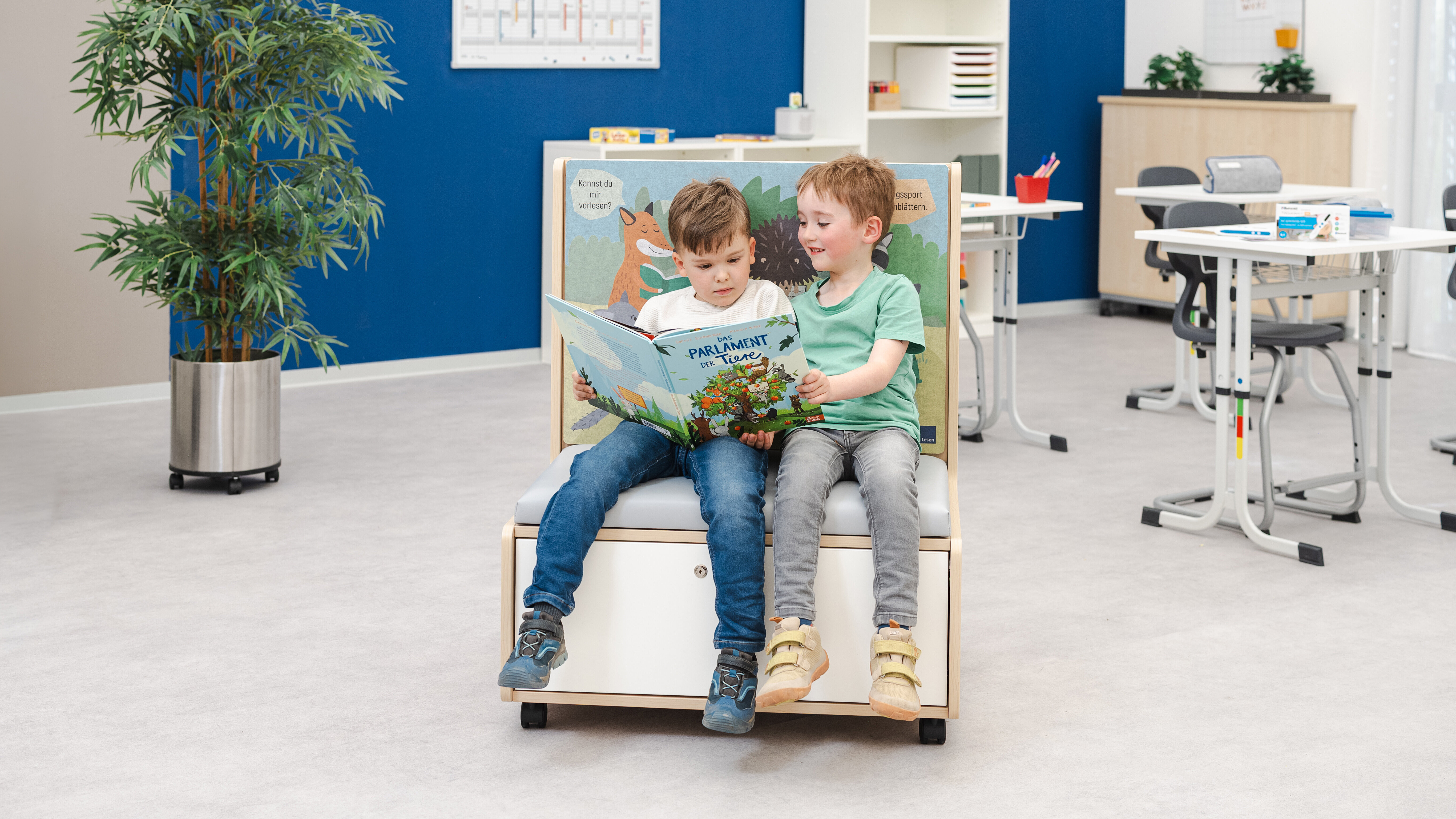 Zwei Kinder sitzen auf einem Lese-Möbel und schauen gemeinsam in ein Buch