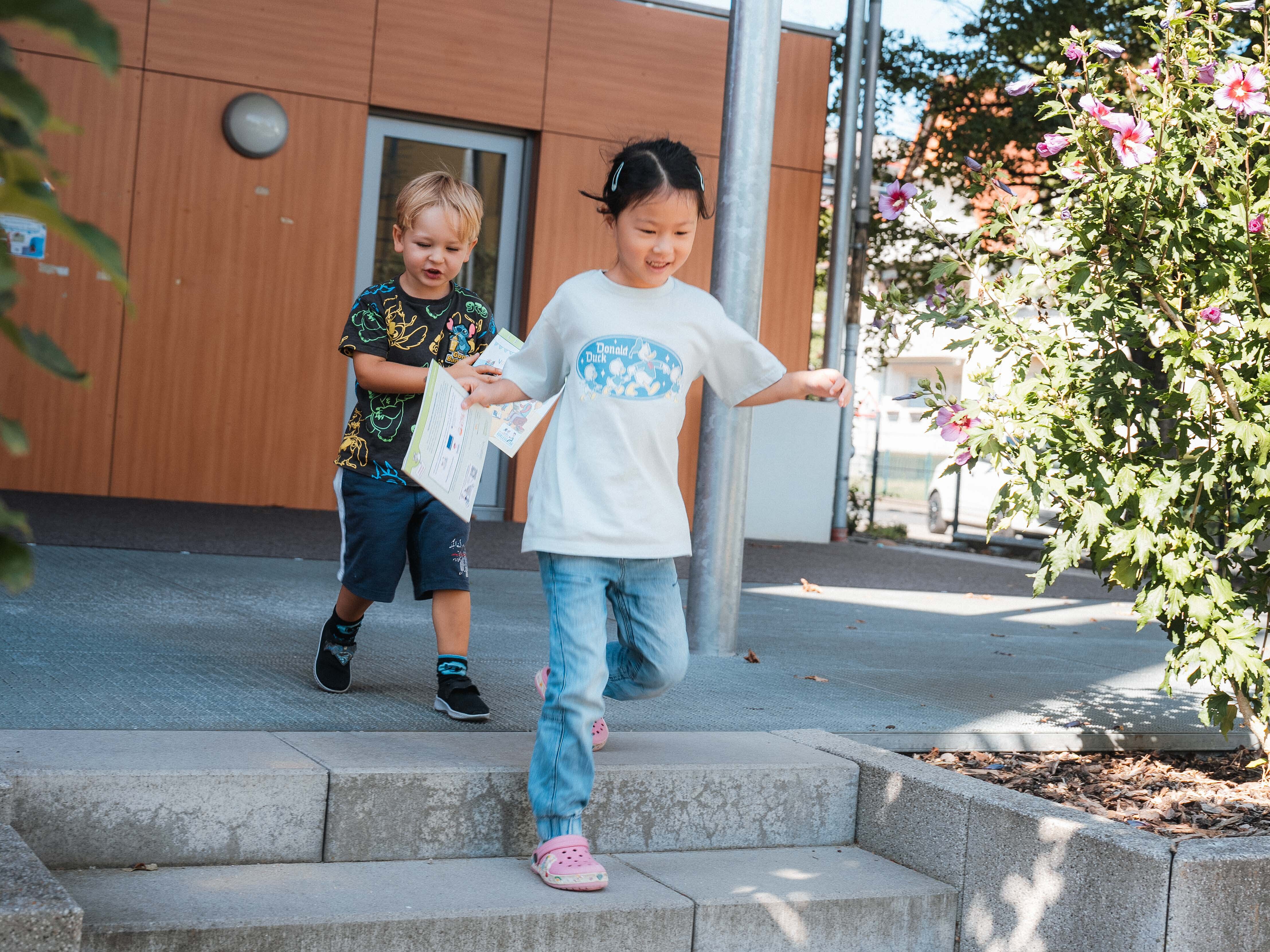 Zwei Kinder laufen schnell Treppen hinab und halten Bücher in der Hand