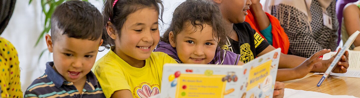 Mehrere Kinder sitzen gemeinsam an einem Tisch und blättern in bunten Bilder- und Lernbüchern in einer pädagogischen Gruppenaktivität.