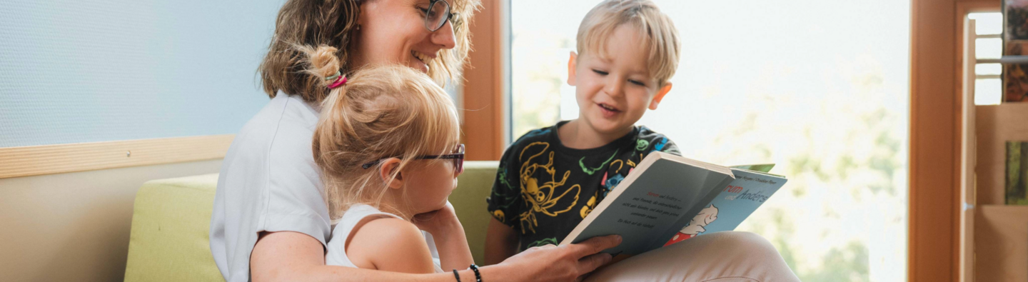 eine Frau liest zwei kleinen Kindern aus einem Buch vor