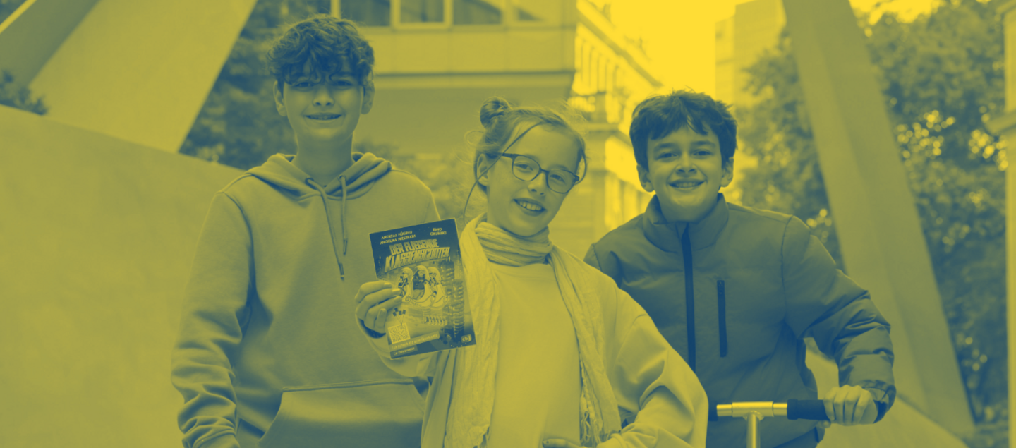 Drei Kinder stehen draußen in einer Stadtumgebung. Das Mädchen in der Mitte trägt ein gelbes Kleid und einen gelben Schal und hält ein Buch mit dem Titel „Klassenfahrt ins Abenteuer“ in die Kamera. Links steht ein Junge mit blauem Hoodie auf einem grünen Scooter, rechts ein Junge in roter Jacke mit einem silbernen Roller. Alle drei lächeln.