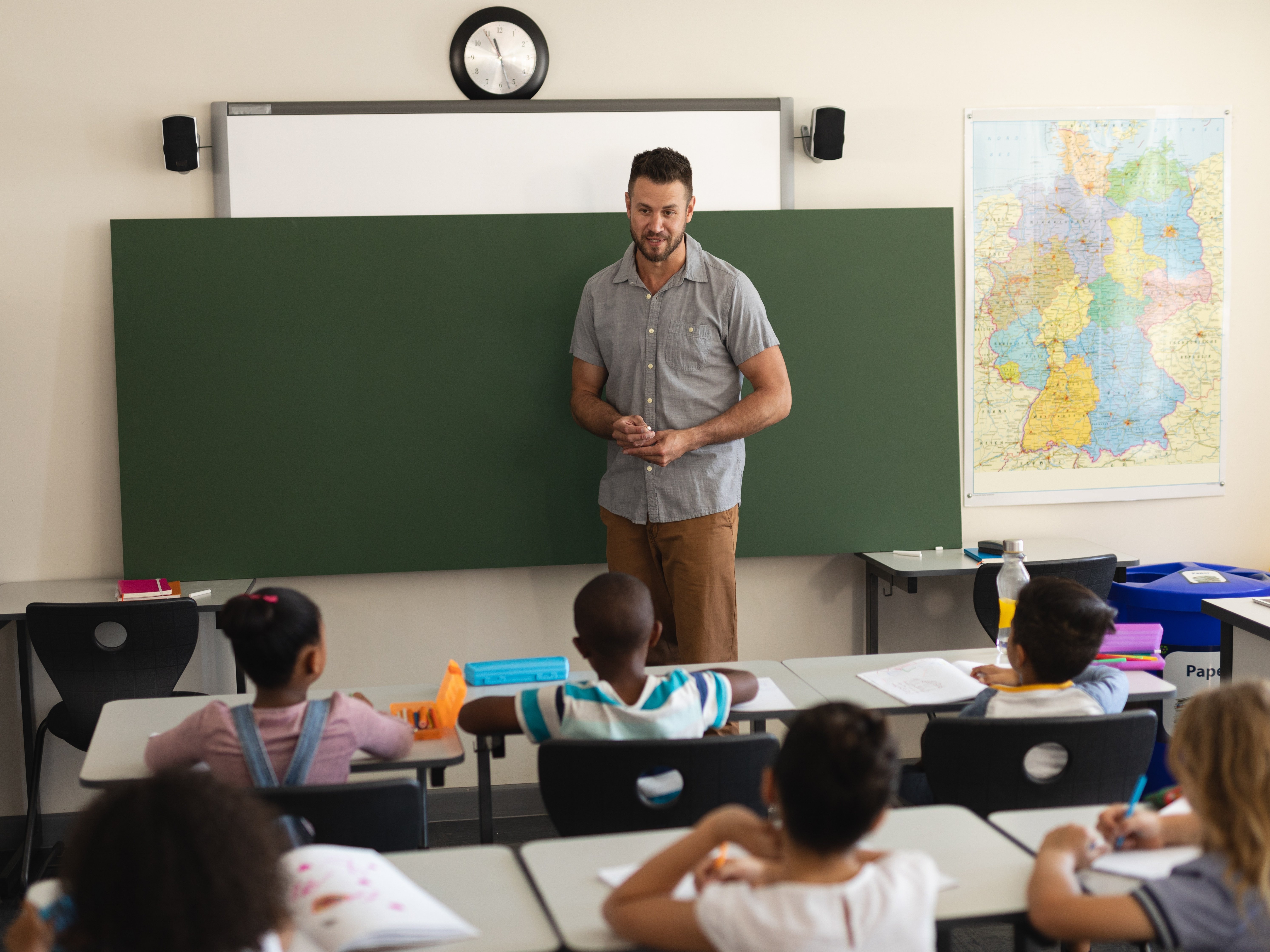 Lehrer steht vor leerer Tafel und spricht mit Grundschulkindern