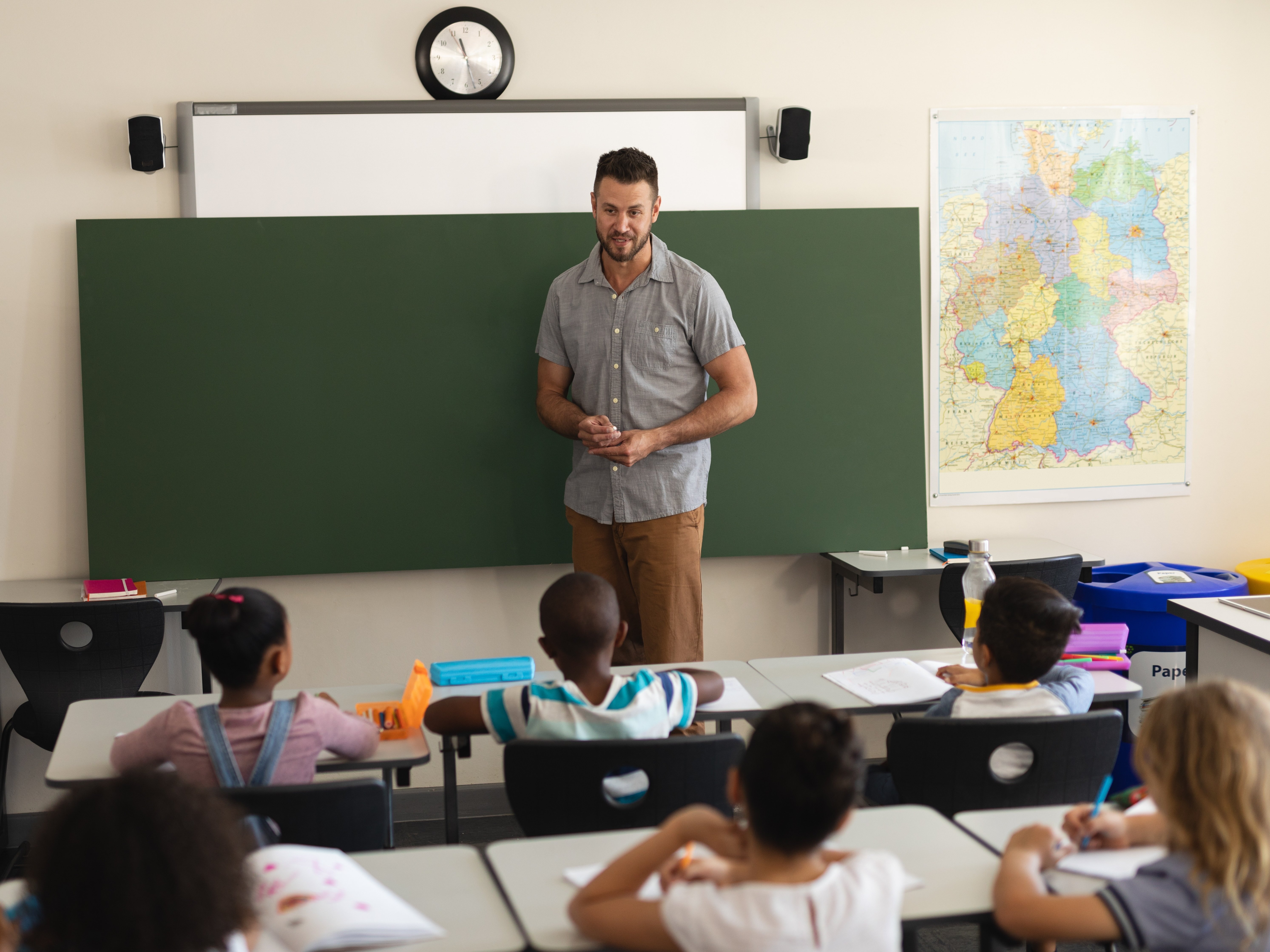 Lehrer steht vor leerer Tafel und spricht mit Grundschulkindern