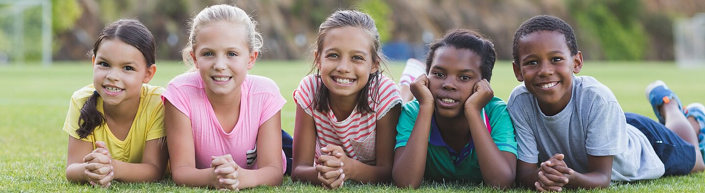 Kinder liegen nebeneinander auf einer Wiese