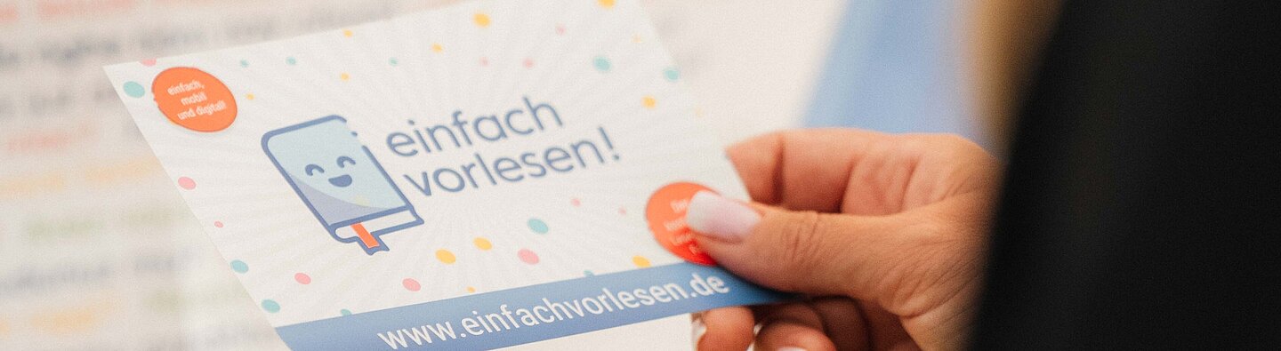 Eine Person hält zwei Karten mit der der Aufschrift einfach vorlesen