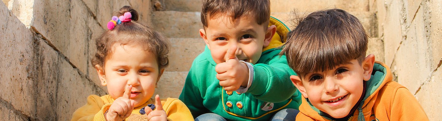 Drei Kinder sitzen auf einer Treppe und gucken in die Kamera