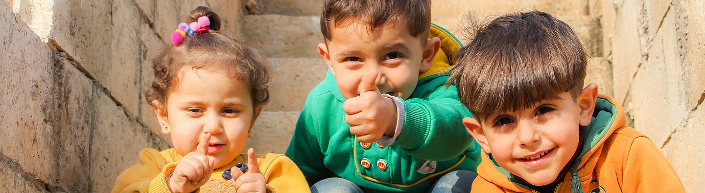 Drei Kinder sitzen auf einer Treppe und gucken in die Kamera