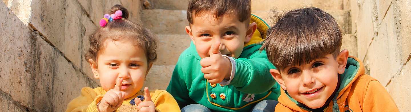 Drei Kinder sitzen auf einer Treppe und gucken in die Kamera