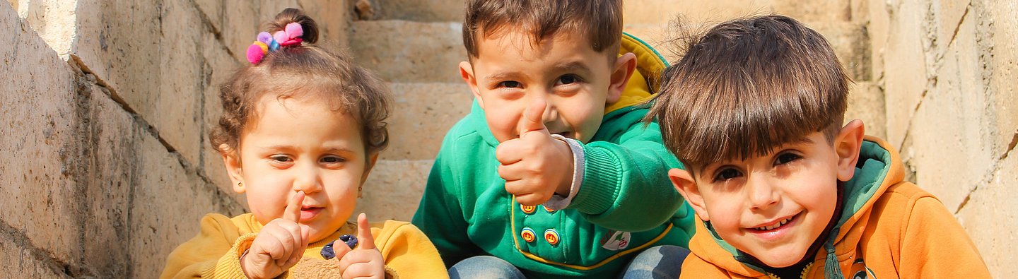 Drei Kinder sitzen auf einer Treppe und gucken in die Kamera