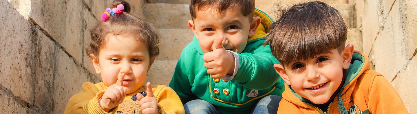 Drei Kinder sitzen auf einer Treppe und gucken in die Kamera