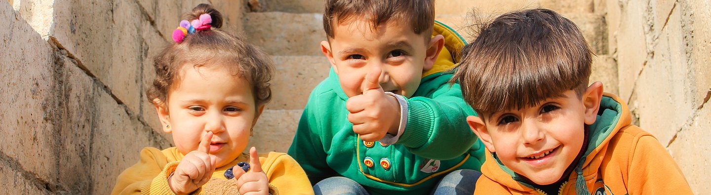 Drei Kinder sitzen auf einer Treppe und gucken in die Kamera