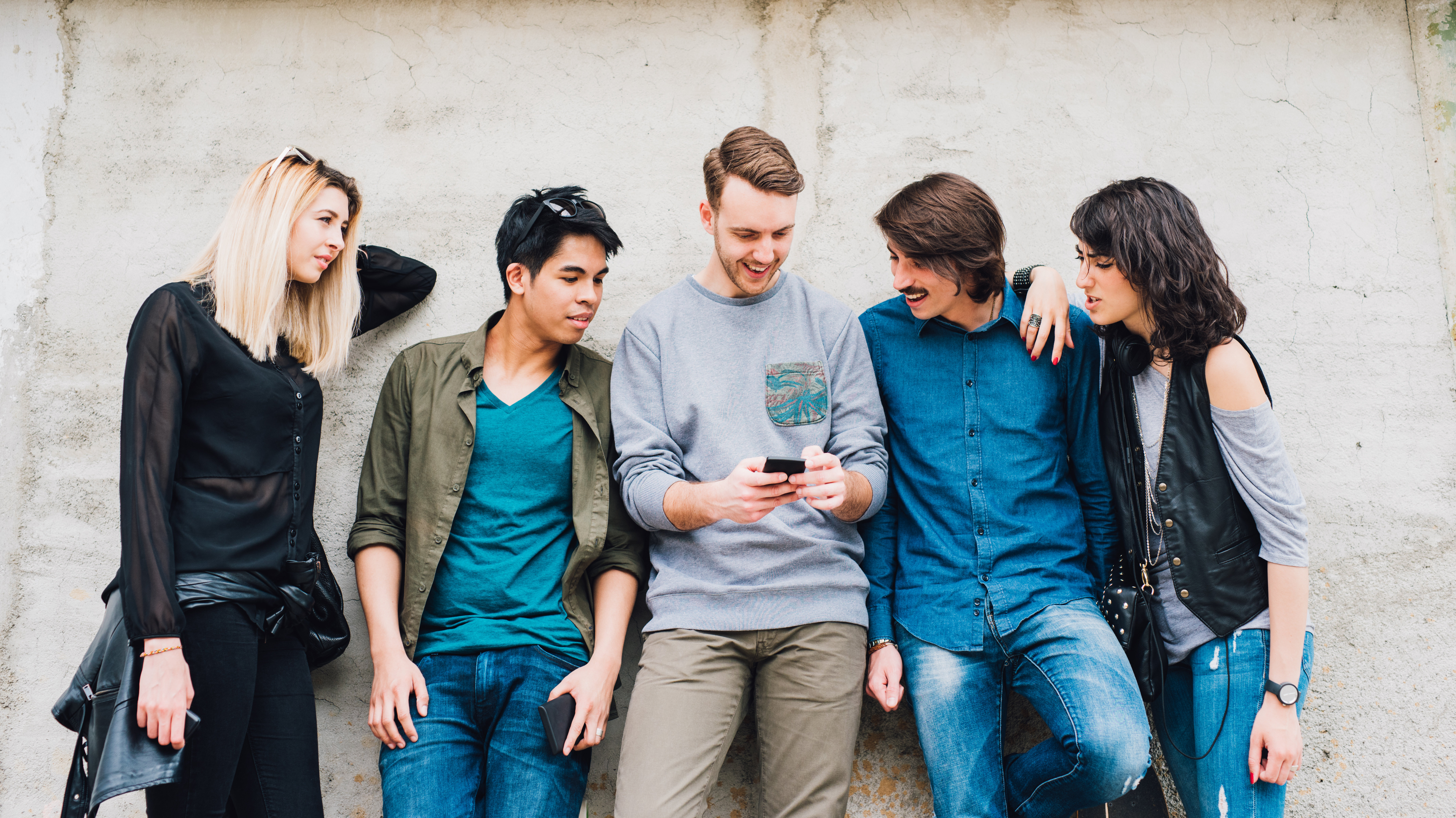 Junge Erwachsene stehen vor Wand und schauen auf Smartphone
