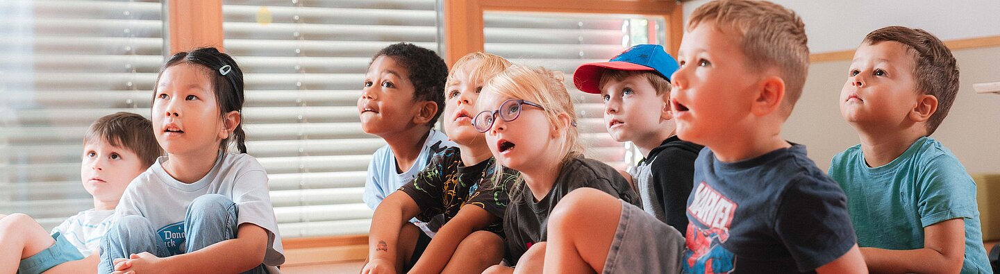 Kinder sitzen auf dem Boden und hören beim Vorlesen zu