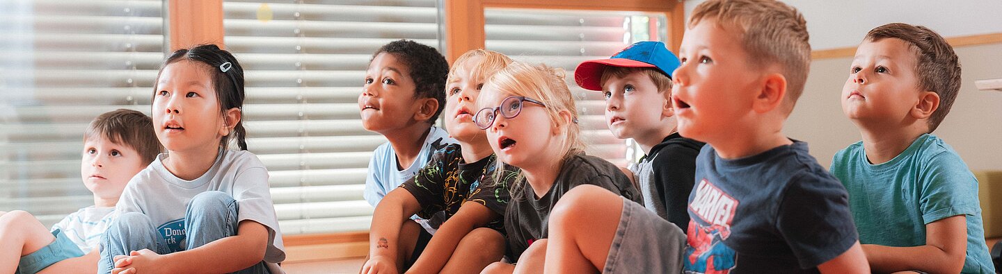 Kinder sitzen auf dem Boden und hören beim Vorlesen zu