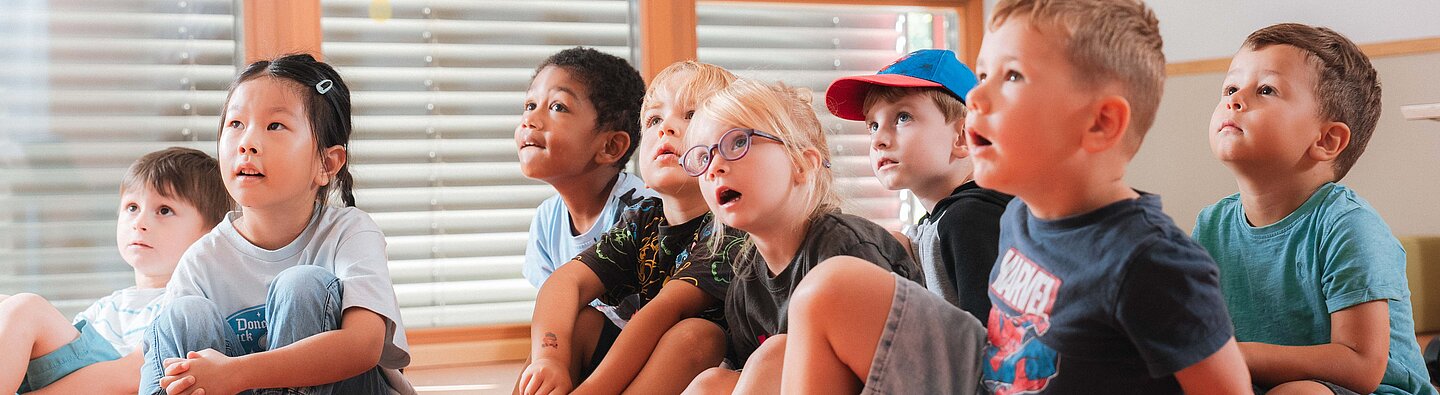 Kinder sitzen auf dem Boden und hören beim Vorlesen zu