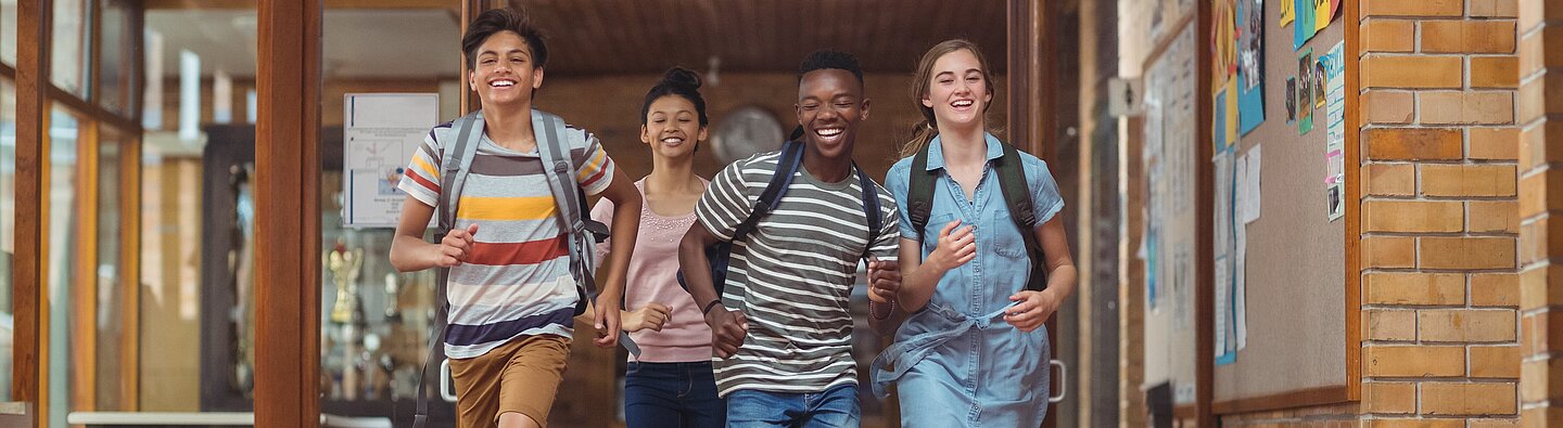 Vier Jugendliche laufen fröhlich aus Schule