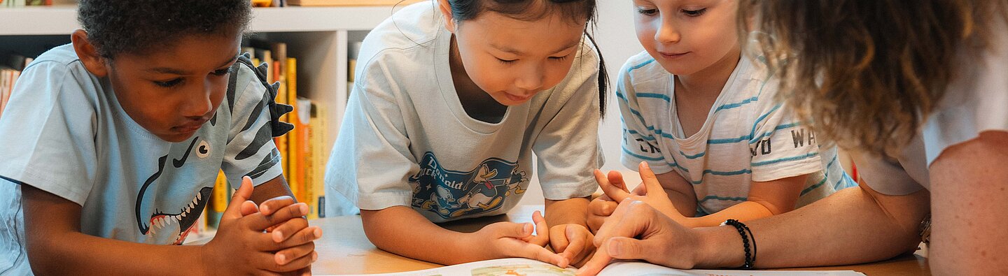 Drei Kinder und eine Kitafachkraft lesen ein Buch